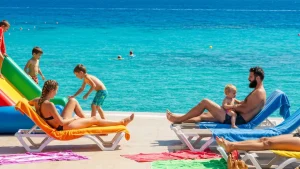 Rodzina z dziećmi na plaży w pobliżu tradycyjnego hotelu na Krecie, baseny dla dzieci i widok na morze Egejskie